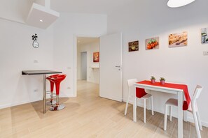 A modern kitchen with a dining area, featuring a white table with a red tablecloth, red bar stools, and a small kitchen island with a black countertop.