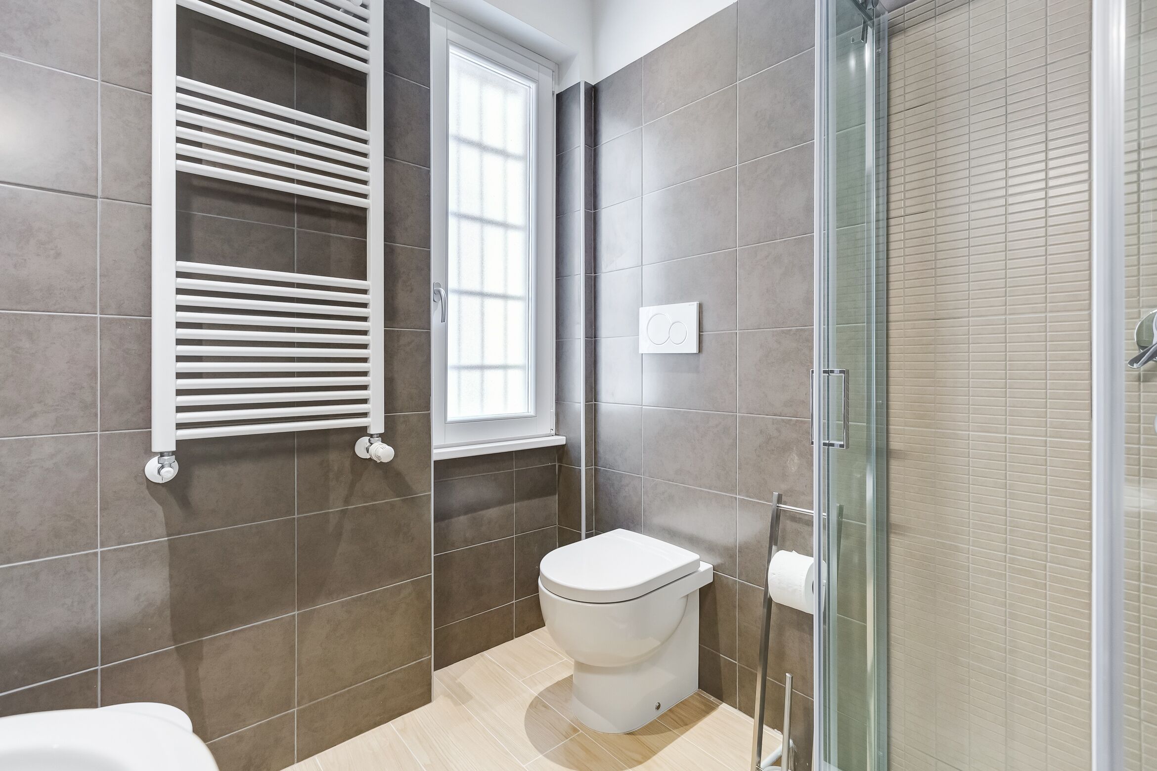 A modern bathroom with a toilet, a glass shower enclosure, and a window providing natural light.