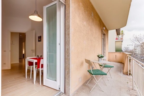 A balcony with a table and chairs, a sliding glass door, and a view of the cityscape.