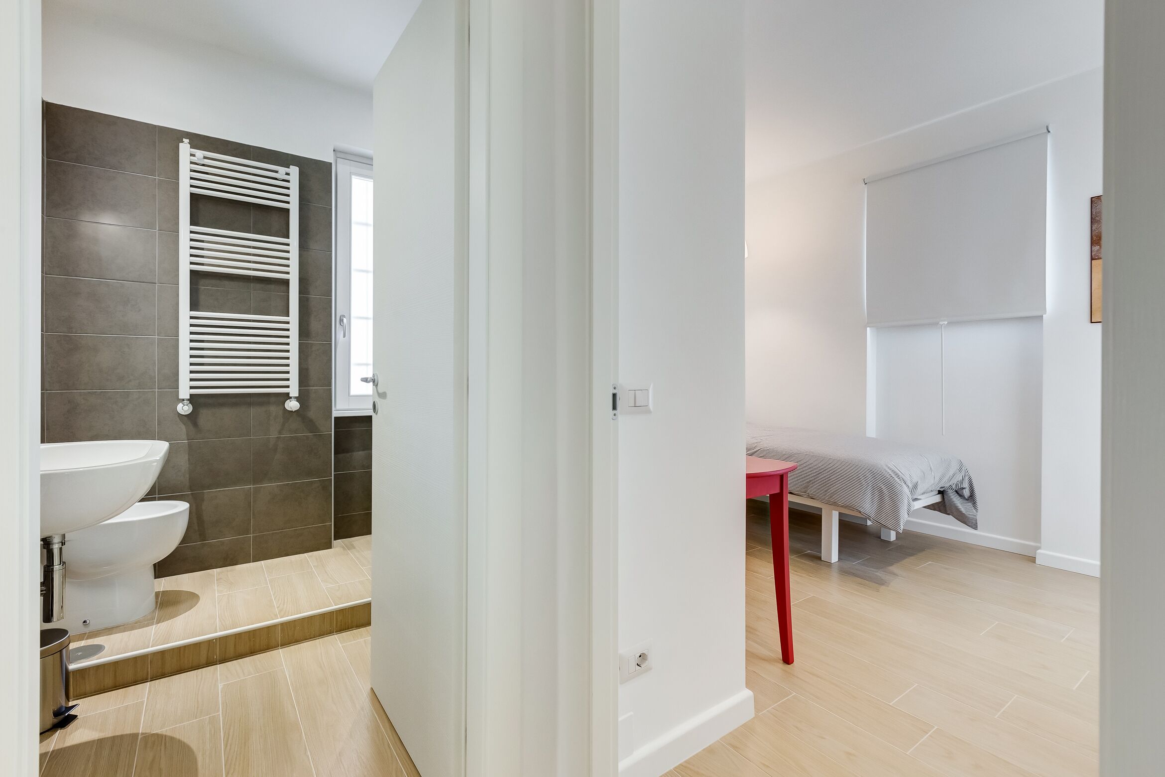A modern bathroom with a white sink, dark tiled walls, and a red chair.