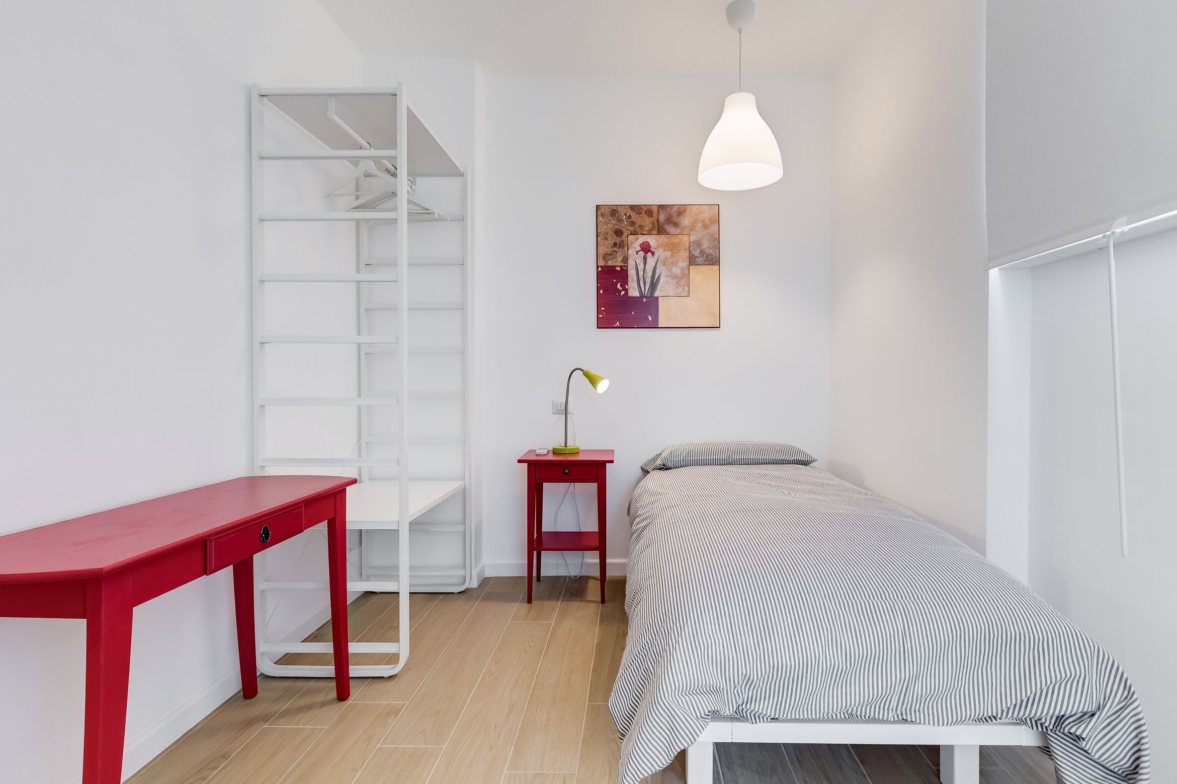 A bedroom with a bed, a desk, a chair, a wardrobe, and a painting on the wall.