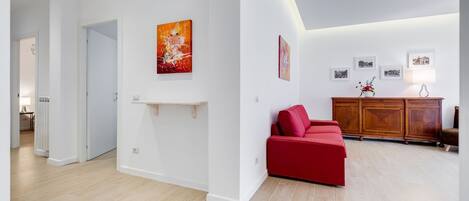 Un salon moderne avec un canapé rouge, un meuble en bois et des œuvres d’art accrochées aux murs.