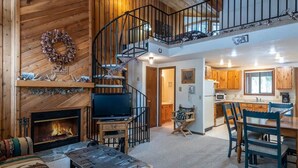 Un interior de cabaña acogedor con chimenea, paredes de madera, televisor, comedor y cocina.
