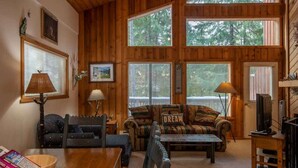 Un acogedor interior de cabaña con detalles de madera, un sofá con una almohada que dice 'DREAM', una mesa de comedor y un televisor.