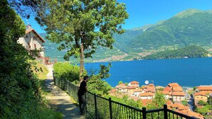 Un sender panoràmic amb una barana metàl·lica que condueix a un llac amb un poble al fons.