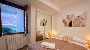 A bedroom with a large bed, a window with a view, a radiator, and a mirror. - RUBINO NEW!  NEAR BELLAGIO! BALCONY GARDEN, &  STUNNING VIEW! (lezzeno)
