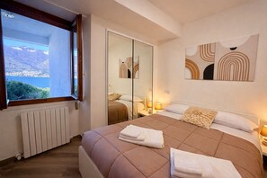 A bedroom with a large bed, a window with a view, a radiator, and a mirror. - RUBINO NEW!  NEAR BELLAGIO! BALCONY GARDEN, &  STUNNING VIEW! (lezzeno)
