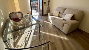 A modern living room with a glass coffee table, a beige sofa, and a view of a mountainous landscape through an open door. - RUBINO NEW!  NEAR BELLAGIO! BALCONY GARDEN, &  STUNNING VIEW! (lezzeno)