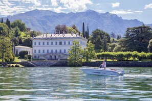 Ein See mit einem Boot, ein großes weißes Gebäude mit vielen Fenstern und Berge im Hintergrund.
