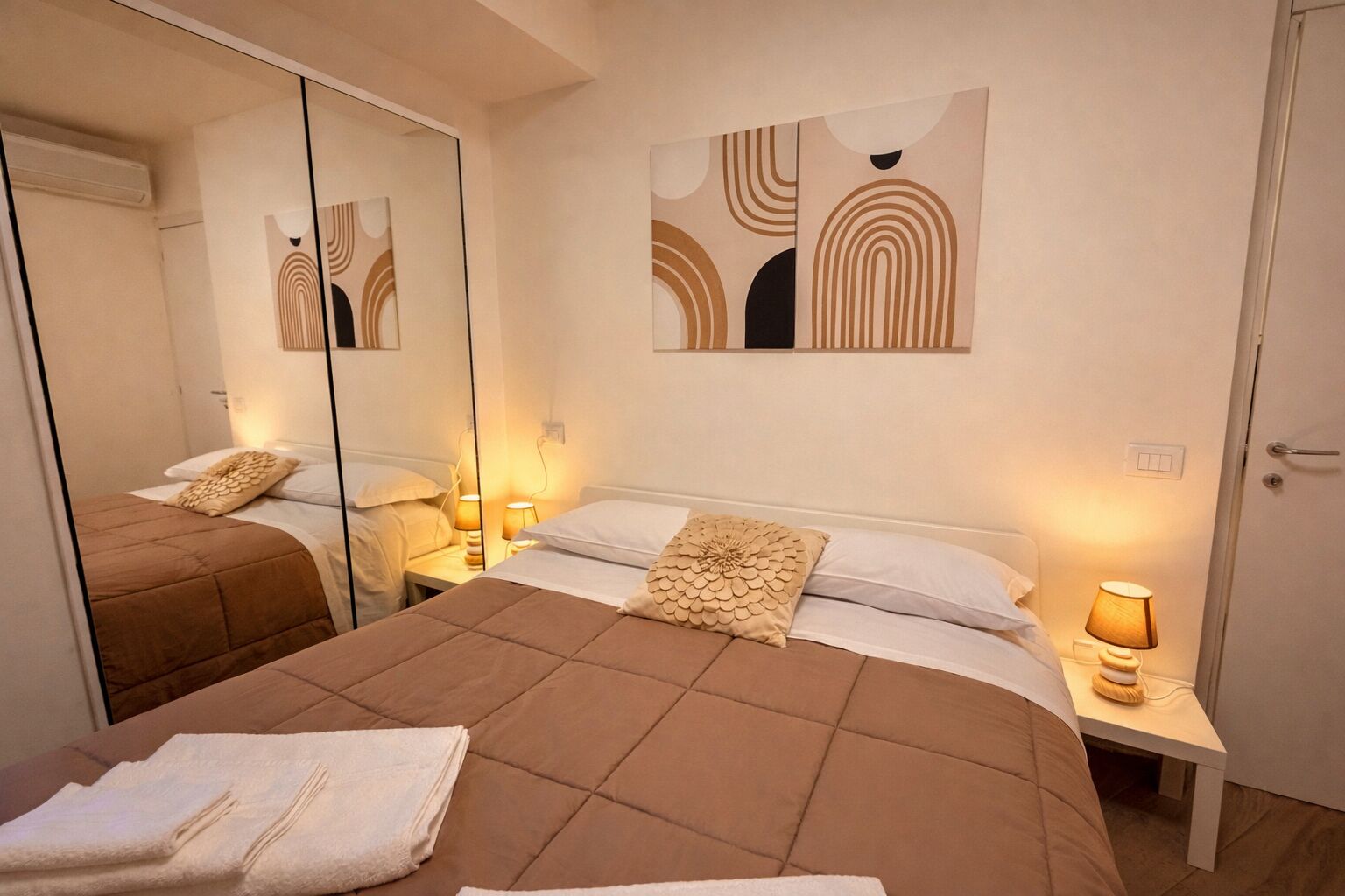 A hotel room with a bed, bedside tables, a mirror, and abstract wall art.