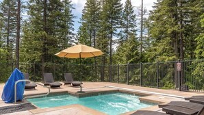 A swimming pool with lounge chairs and an umbrella, surrounded by a fence and trees. - Escape to Ptarmigan Village 79 (Whitefish)