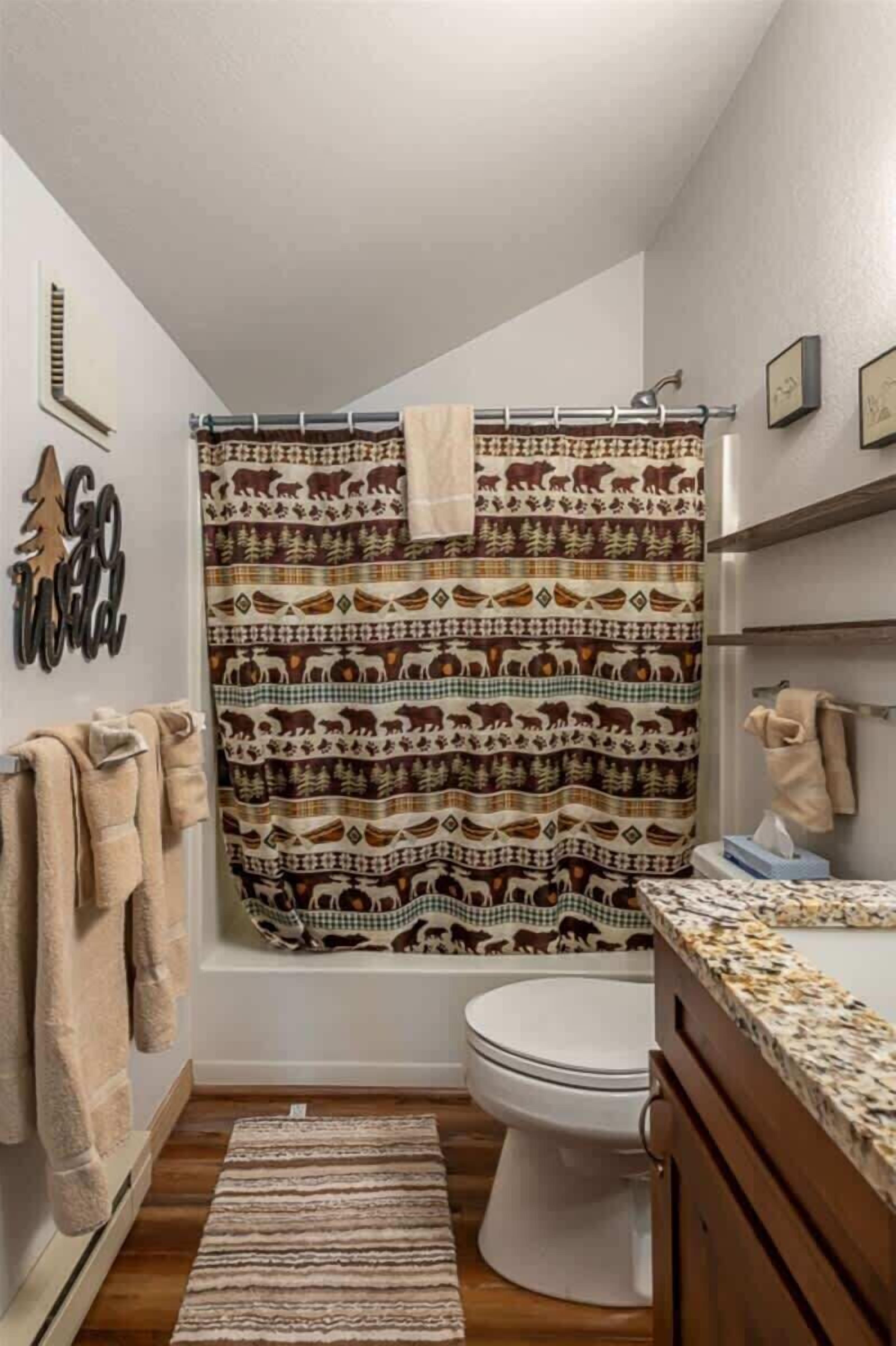 A bathroom with a patterned shower curtain, a toilet, a sink with a countertop, and a rug on the floor.