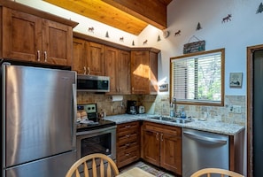 A kitchen with wooden cabinets, stainless steel appliances, a window with blinds, and a welcome sign.