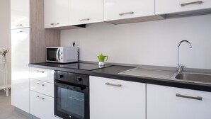 A modern kitchen with white cabinets, a black countertop, a built-in oven, a microwave, a green kettle, and a stainless steel sink. - Luxury Seafront Dependance in Fertilia (Fertilia)