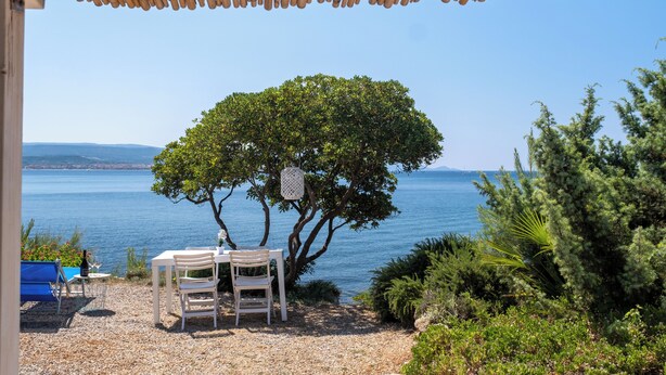 A table and chairs under a bamboo pergola overlooking a body of water with a tree in the foreground. - Luxury Seafront Dependance in Fertilia (Fertilia)