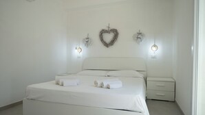 A modern bedroom with a large bed, two bedside tables, and decorative wall hangings. - Luxury Seafront Dependance in Fertilia (Fertilia)