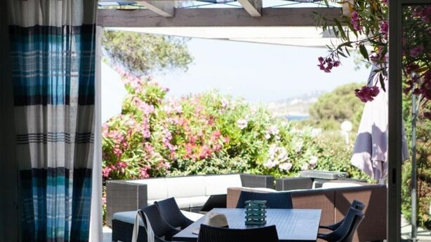 An outdoor patio with wicker furniture and a table, overlooking a garden with pink flowers. - House in a residence for 8 person (s) - Lumio (St Ambroggio Lumio)