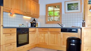Ett kök med träskåp, en inbyggd ugn, en diskmaskin, ett fönster med utsikt över grönområden och en soptunna.