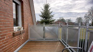 A wooden deck with a brick wall, a window, and a Christmas tree. - Apartment Noerdliches Muensterland (Hopsten)