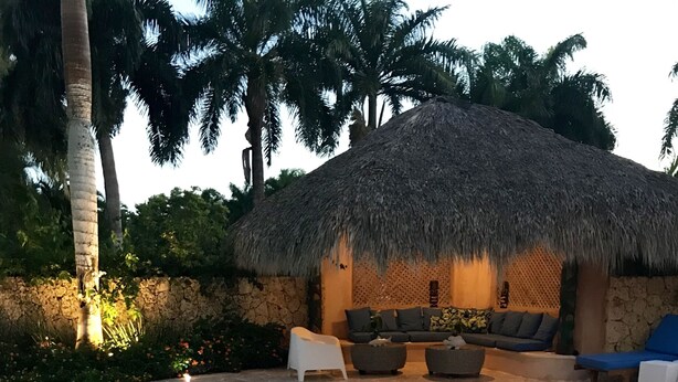 A pool area with a thatched-roof structure, lounge seating, and a dining table with plates and a potted plant. - 120 +5 STAR reviews below 3 Min to Beach English speaking Chef  Butler Meal Plan (La Romana)