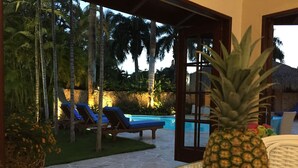A poolside area with lounge chairs, a pineapple, and oranges on a table. - 120 +5 STAR reviews below 3 Min to Beach English speaking Chef  Butler Meal Plan (La Romana)