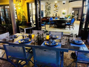 Un comedor con mesas dispuestas para una comida, sillas y vista de la habitación contigua.