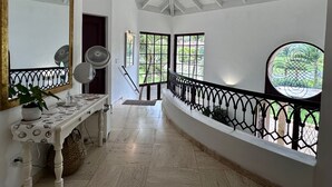 A hallway with a high ceiling, a white wall, a wooden bench, a mirror, a fan, and a view of greenery outside. - 120 +5 STAR reviews below 3 Min to Beach English speaking Chef  Butler Meal Plan (La Romana)