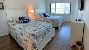 Een slaapkamer met twee bedden, een televisie en een raam met zonwering.