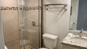 Een badkamer met een douche met glazen wand, een toilet, een wastafel met een granieten aanrechtblad en een spiegel boven de wastafel.
