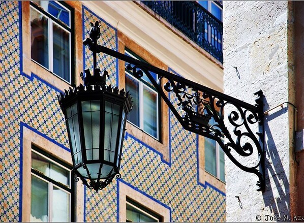 Una farola tradicional con diseño decorativo, adosada a un edificio con fachada ornamentada.
