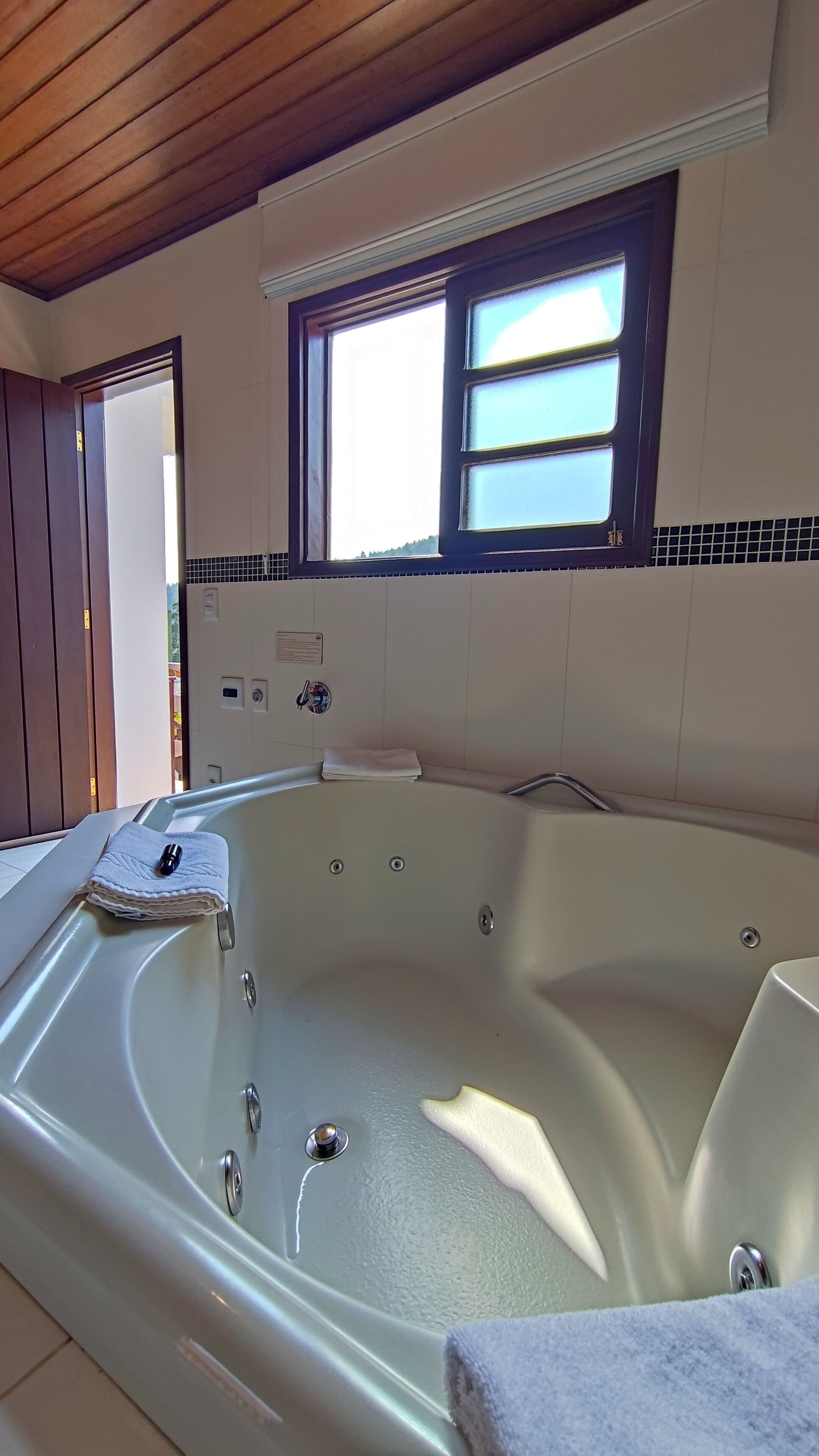 A large, empty bathtub with a window above it, a towel on the edge, and a wooden ceiling.