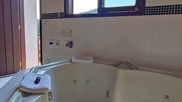 A large, empty bathtub with a window above it, a towel on the edge, and a wooden ceiling.