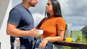 A couple on a balcony with breakfast items, including bread, a bowl of fruit, and a bottle of orange juice.