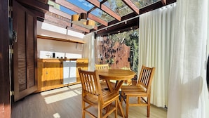 Una mesa de comedor de madera con sillas, una zona de cocina con armarios de madera y vistas a zonas verdes a través de un ventanal.