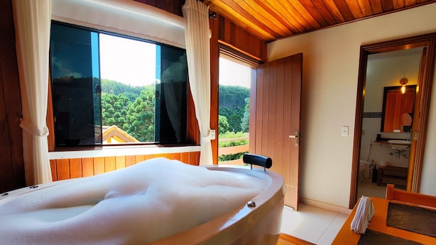 Un baño con suelo de madera, bañera, lavabo y ventana con cortinas.
