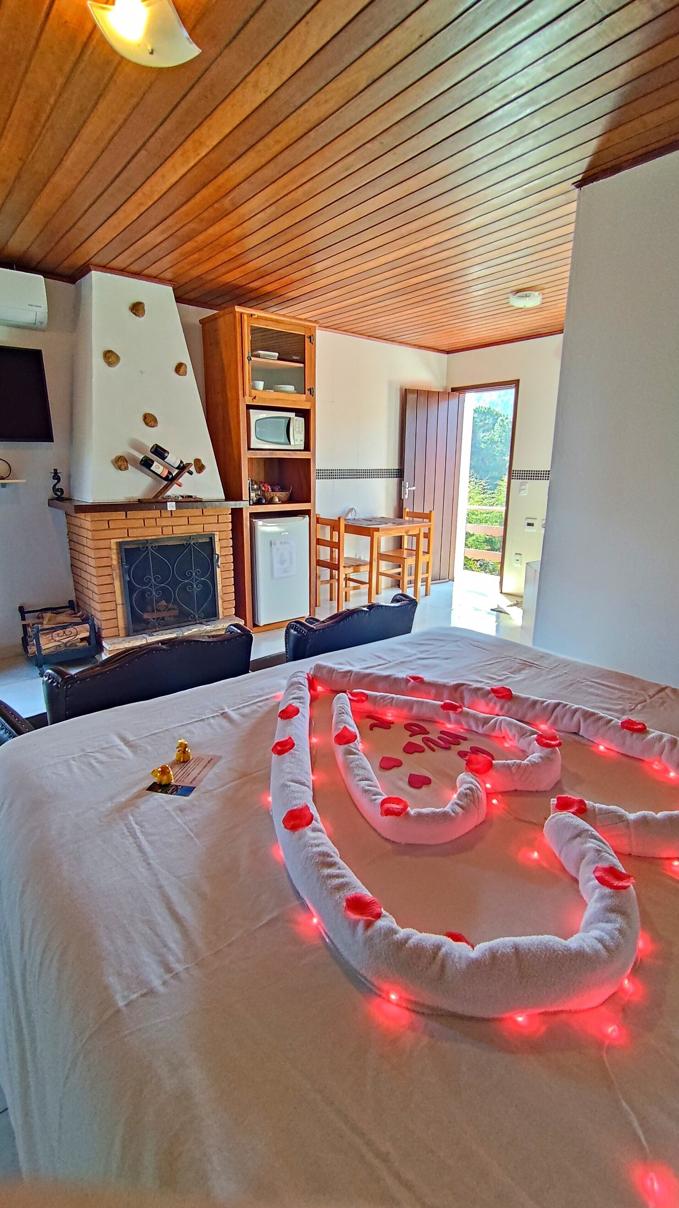 A cozy room with a fireplace, a dining area, and a bed with rose petals and lights.