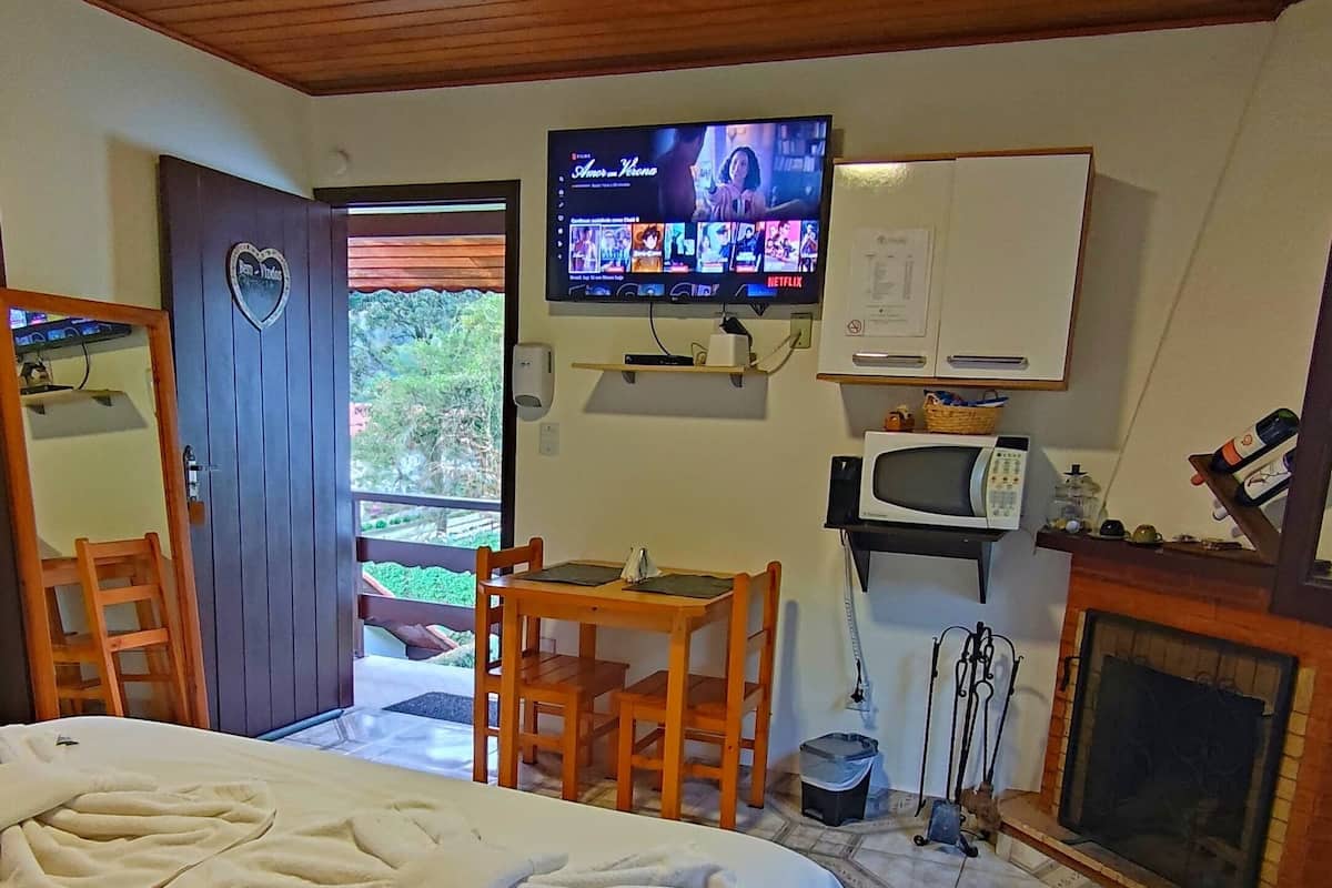 A bedroom with a large bed, a television mounted on the wall, a small table, and a fireplace.