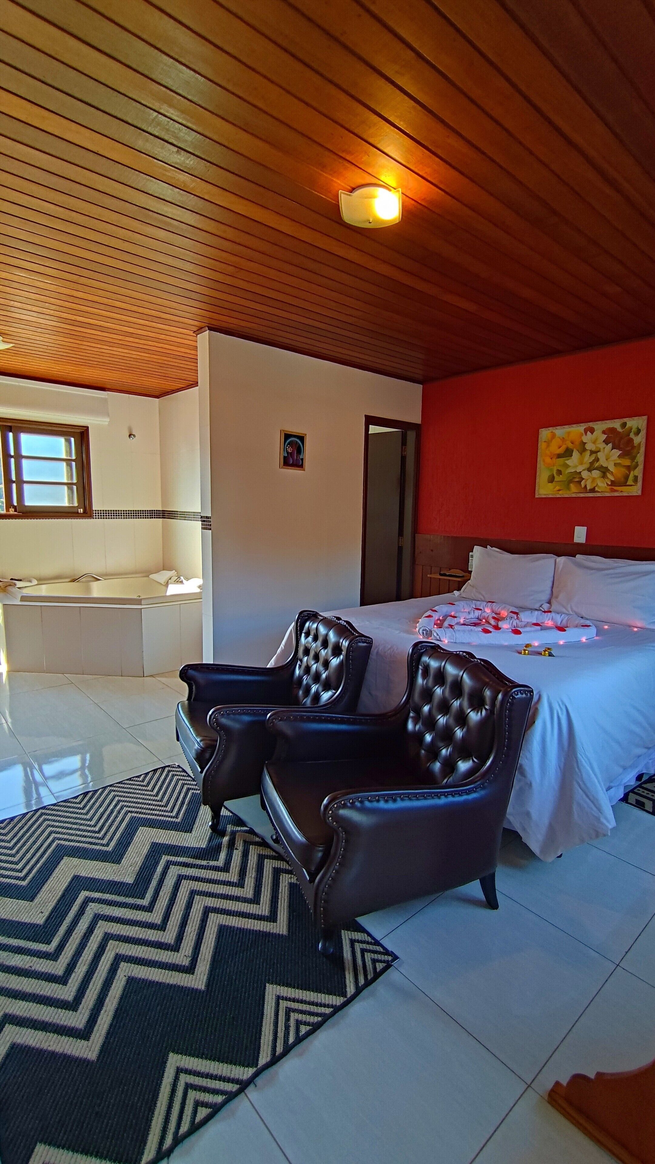 Een slaapkamer met een groot bed, twee leren fauteuils, een houten plafond, een rode wand en een schilderij.