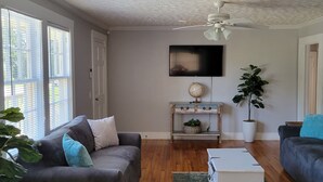 A living room with a grey sofa, a white coffee table, and a TV on the wall.