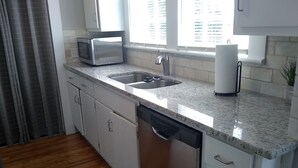 A kitchen with white cabinets, a granite countertop, a microwave, a sink, and a dishwasher.