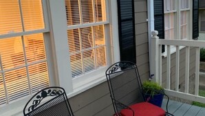 A porch with two metal chairs with red cushions, a potted plant, and a white railing.