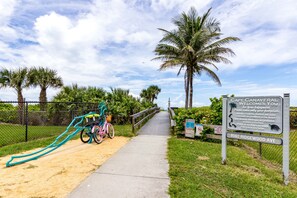 A pathway leading to a beach area with a sign indicating 'Cape Canaveral Welcomes You' and a beach crossing warning.