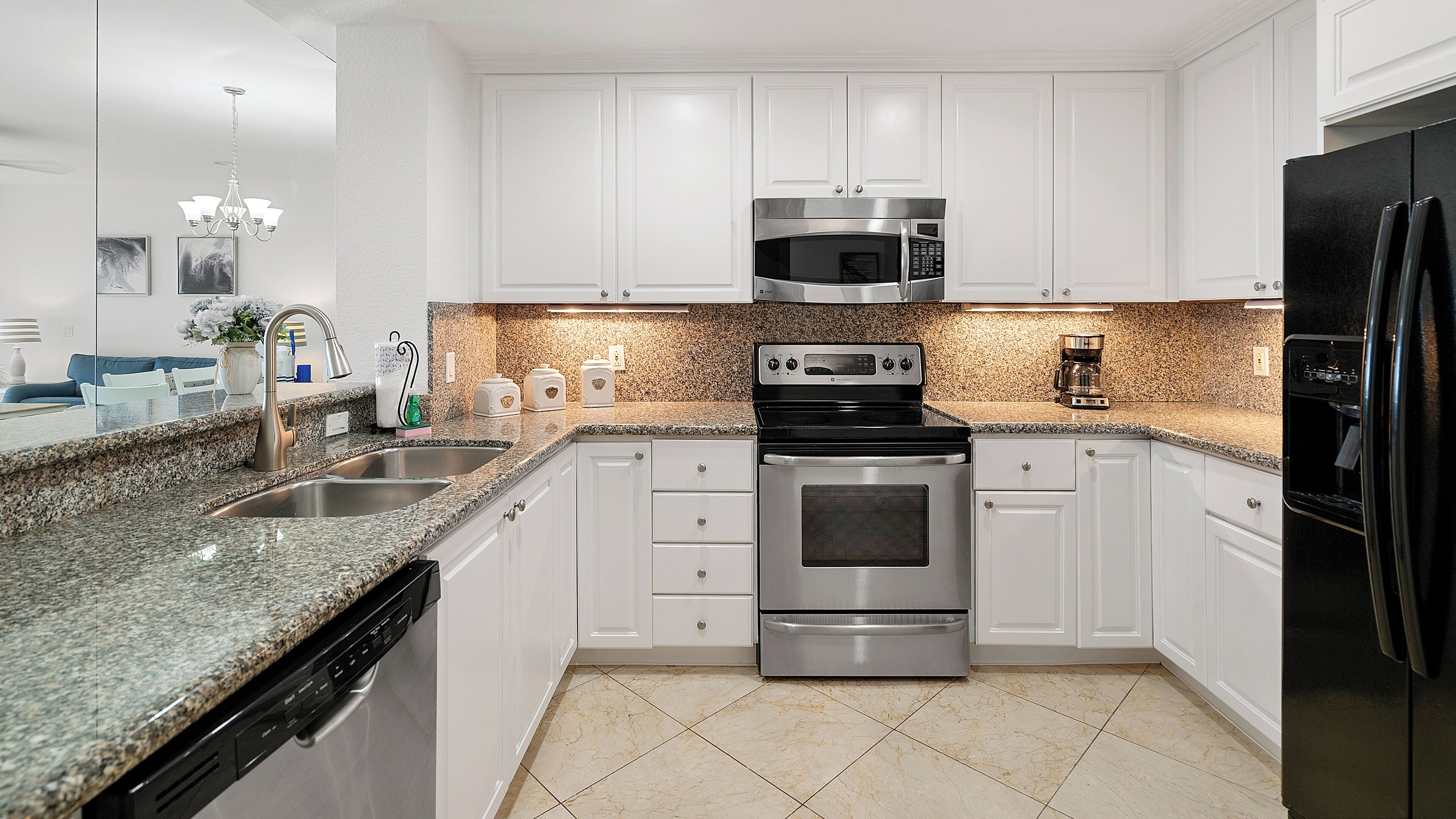 Uma cozinha moderna com armários brancos, eletrodomésticos de aço inoxidável, bancadas de granito e piso cerâmico.