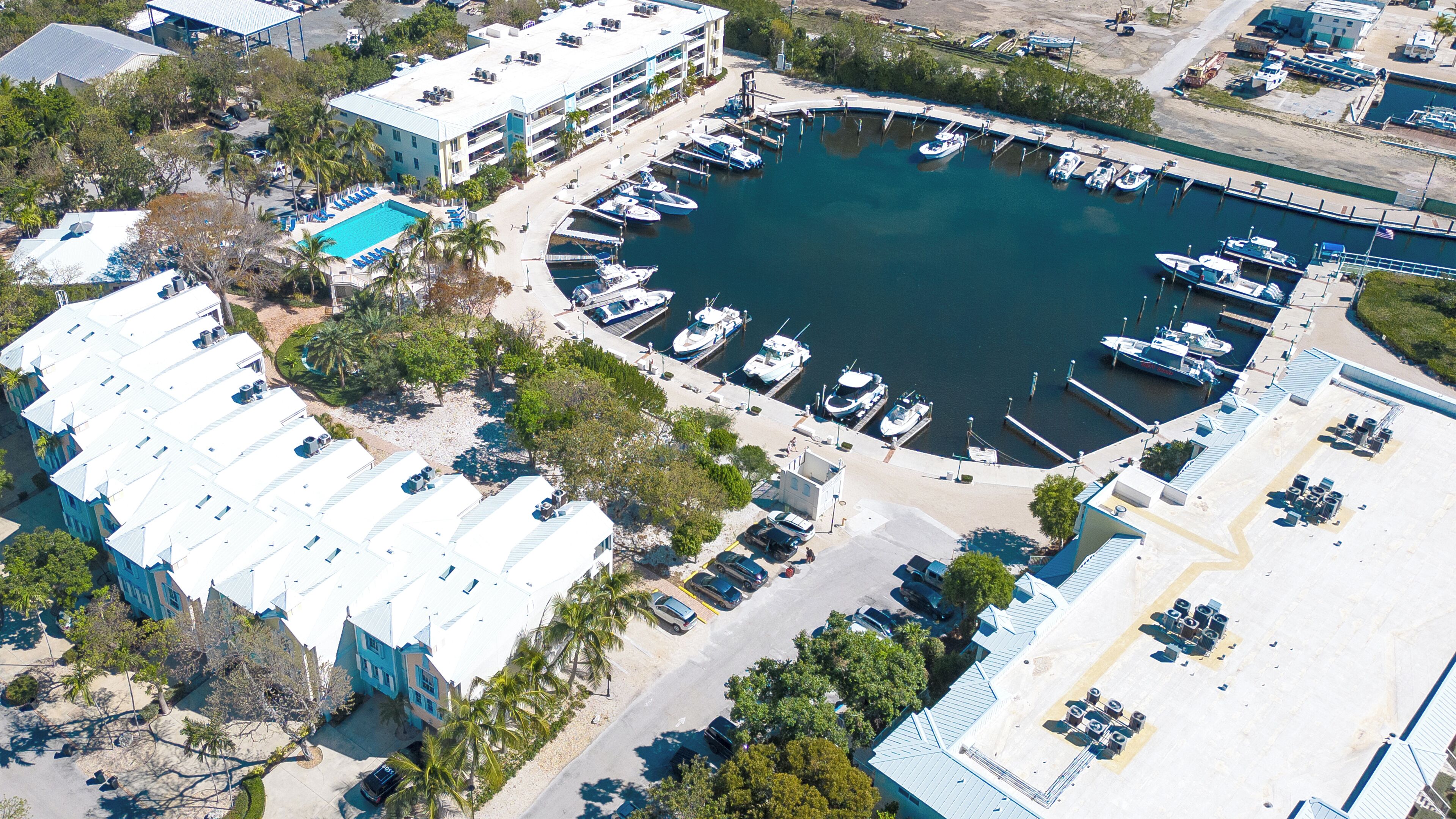 Vista aérea de un puerto deportivo con barcos amarrados, una piscina y edificios cercanos con un estacionamiento.