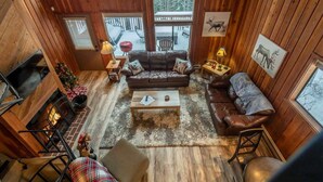 Een gezellig cabin interieur met een open haard, leren banken, een bijzettafeltje en uitzicht op een besneeuwd terras.