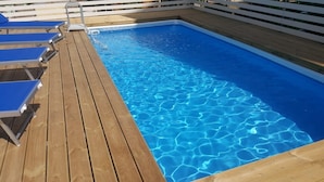 A wooden deck with a swimming pool, blue lounge chairs, and a white fence. - Casa Raffaella - Apartment 2 (Pimonte)