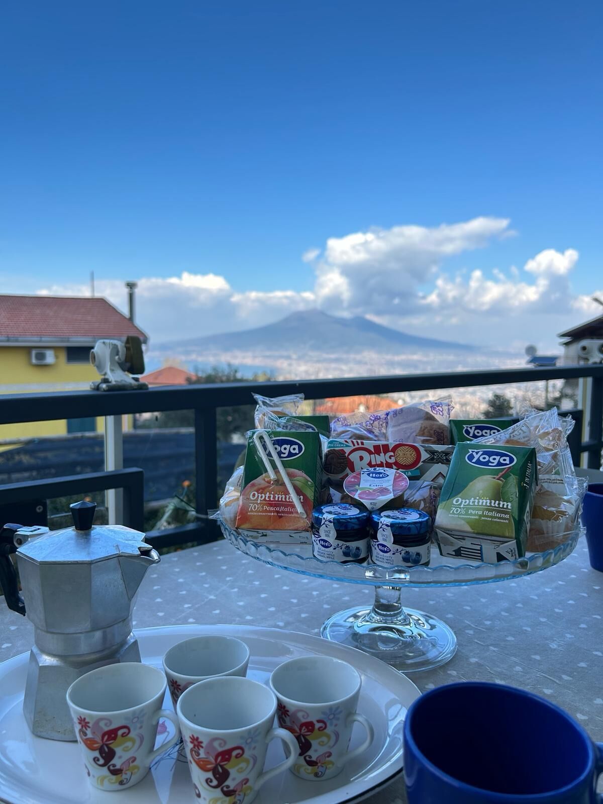 Un balcone con un tavolo apparecchiato per la colazione, comprensivo di caffettiera, tazze e alimenti confezionati.