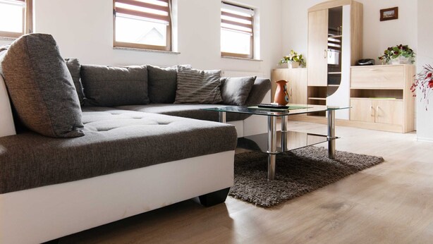 Una sala de estar moderna con un sofá seccional, una mesa de centro de vidrio y un mueble de madera.