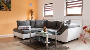 Una sala de estar moderna con un sofá seccional, una mesa de centro de vidrio y dos ventanas con persianas.