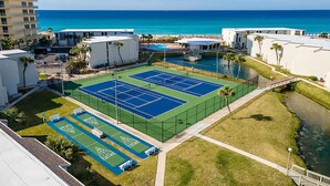 Una pista de tennis envoltada d'edificis, una piscina i una vista de l'oceà.